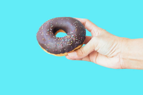 istock Chocolate donuts hand holding isolated on blue background 1285726671