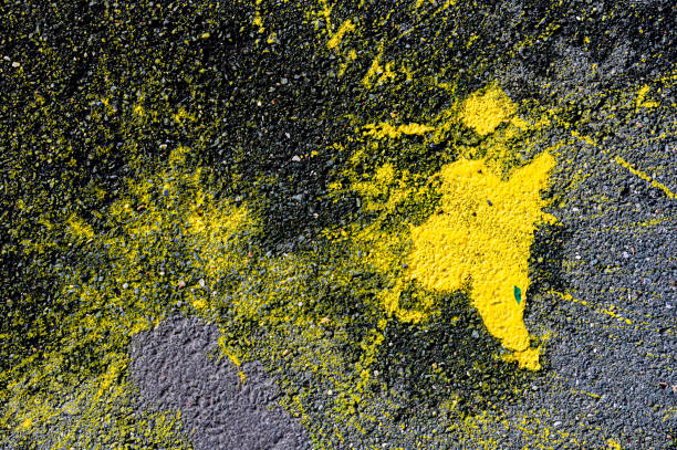Abstract pattern formed by random spots and splashes of yellow paint on cracked black asphalt.