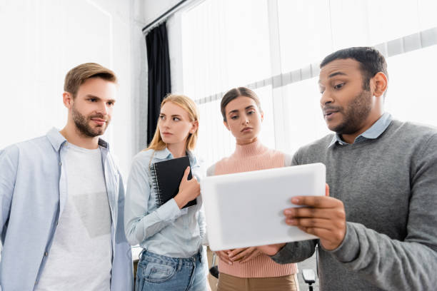 istock Indian businessman holding digital tablet near colleagues with notebook in office 1285738549