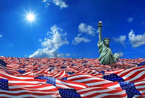 Conceptual image of large group of American flags and Statue of Liberty over clear blue sky.