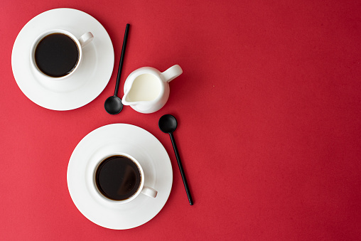 black coffee in small coffee cup and milk jug on red background, top view