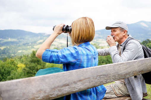 Young woman observing nature with binoculars and her father taking a sip of coffee