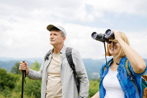 istock Happy young woman standing by a senior man holding trekking pole and using binoculars 1285752328