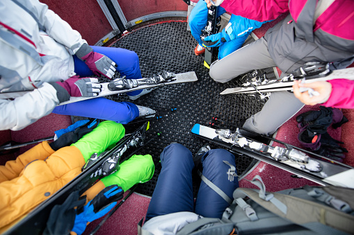 Family is sitting in round ski lift gondola. Shot if legs and skis from above.
Nikon D850