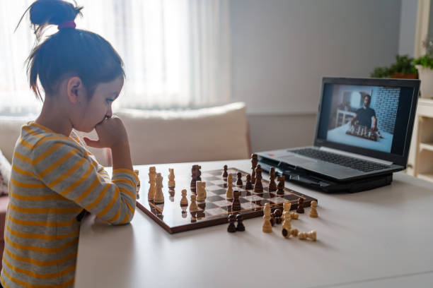 brillante niña jugando ajedrez con su pariente distante o tío, utiliza el ordenador portátil para la videollamada. educación remota en línea, e-education, comunicación con la familia, educación en el hogar - chess skill concentration intelligence fotografías e imágenes de stock