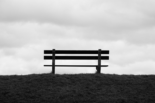 Park bench facing clouds black and white