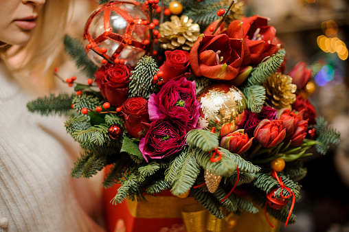 Close-up view of flower arrangement of bright red flowers and fir branches decorated with New Year's toys in women's hands