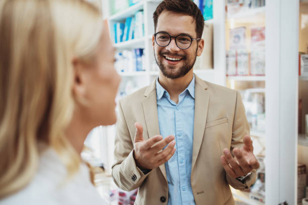 Business man in pharmacy store Young business man choosing and buying drugs in a drugstore while talking with attractive female pharmacist. She helping him with expert advices. salesman stock pictures, royalty-free photos & images