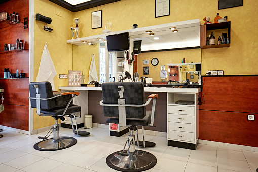 Rear view of two styling chairs facing vanity mirrors and countertop with tools of the trade in hair salon.