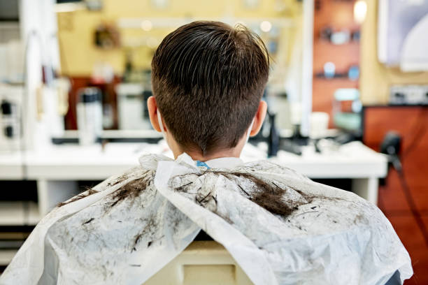 Rear Portrait of Fresh Male Haircut in Modern Salon Rear view of 14 year old Caucasian boy with brown hair sitting in stylist chair wearing cape after receiving haircut. teenager boy haircuts stock pictures, royalty-free photos & images