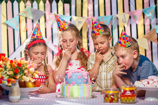Little children rejoice on girl's birthday, testing cake and licking cream on fingers
