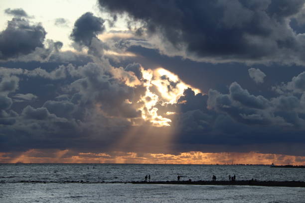 海の夕日を背景に中央に光線を持つ暗い雲。黒いシルエットの人 - today tomorrow yesterday time ストックフォトと画像