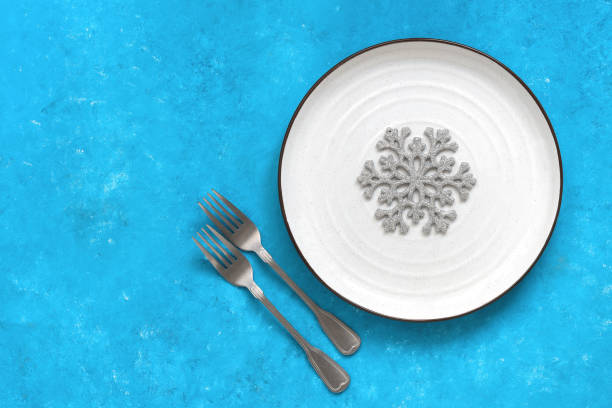 istock Christmas creative table setting. Empty white plate with snowflake and forks on a blue painted background. Top view, flat lay, copy space. 1285778182