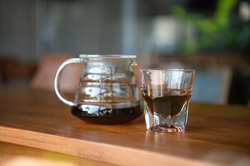 The barista serves hot black coffee in a mugs which making drip coffee by pouring spills hot water on coffee bean.