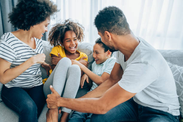 Happy family at home. Cheerful parents having fun while tickling their two kids on sofa in the living room. family at home stock pictures, royalty-free photos & images