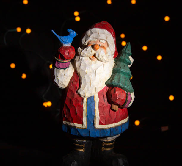 istock Santa clause figurine with blue bird on hand and a pine tree in the other hand. light points in the black background 1285785378