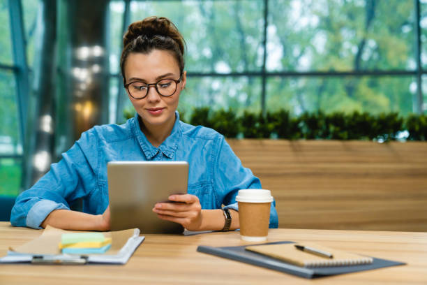 jeune femme d’affaires caucasienne gentille utilisant la tablette au bureau dans le bureau moderne - lire photos et images de collection