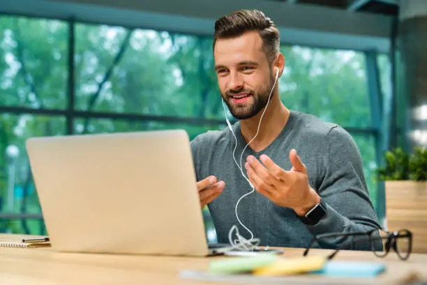 Photo of Attractive 30s caucasian businessman having online conversation using laptop and headphones at office desk