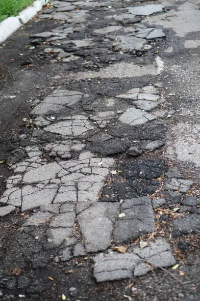 Photo of Destroyed road in poor condition requiring repair. Holes in the asphalt are filled with water and puddles. Stock photo background