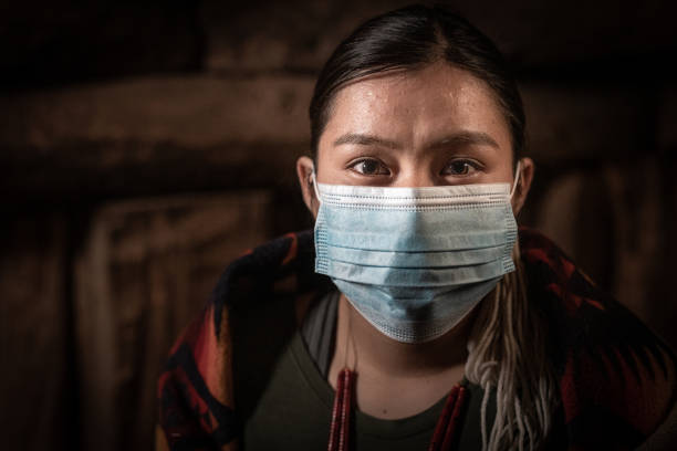 A Fine Art Portrait Of A Beautiful, Serious Native American Young Woman Staying Warm In The Hogan, Wearing A Protective Mask During A Lockdown A Fine Art Portrait Of A Beautiful, Serious, Fearful, Native American Young Woman Staying Warm In The Hogan, Wearing A Protective Mask During  A Lockdown navajo nation covid stock pictures, royalty-free photos & images