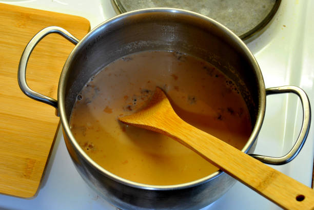 istock Step-by-step instructions for making masala tea: step five - add a glass of milk to boiling water with ginger, black tea and masala mixture and bring to a boil, stirring with a spoon 1285792891