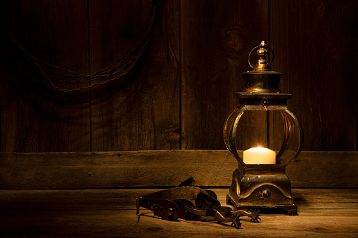 Rusty, old, cobwebbed and dusty kerosene lamp prepared for Halloween. A bright fire burns through the smoky, dusty glass. Dark rag background. Selective focus.