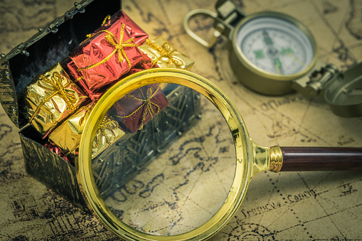The treasure hunt. A magnifying glass and a compass next to a chest full of treasures. Old map, Vintage style