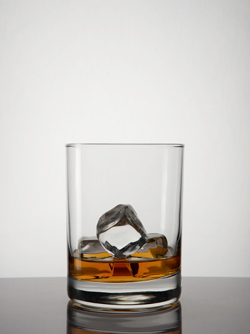 Pouring square crystal decanter with scotch tape whiskey or brandy in a crystal round glass with ice on a blue gradient background with reflection. Copy space
