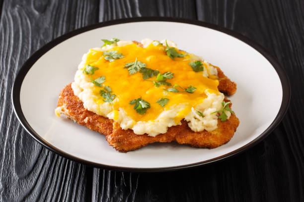 Breaded chicken Parmo baked with bechamel sauce and cheddar cheese close-up in a plate. horizontal Breaded chicken Parmo baked with bechamel sauce and cheddar cheese close-up in a plate on the table. horizontal teesside northeast england stock pictures, royalty-free photos & images