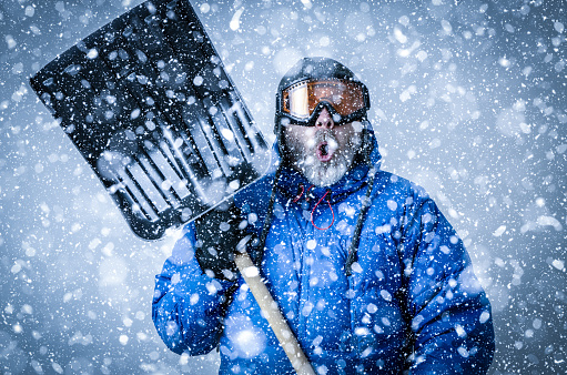 Man with goggles, tuque, winter coat holding a shovel during snowstorm