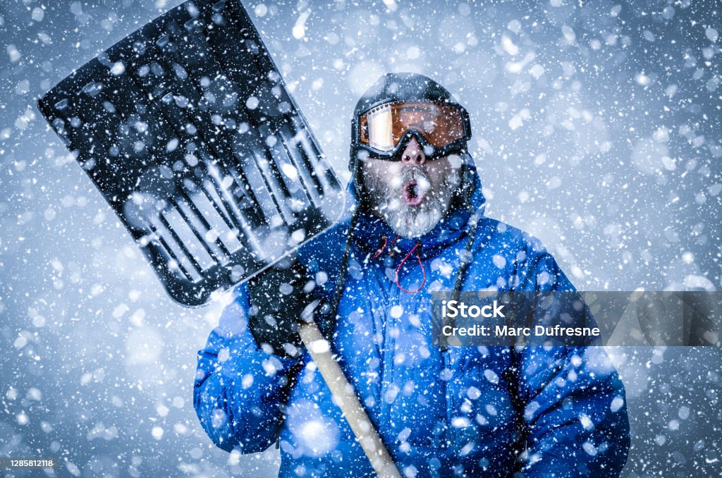 Man with goggles and shovel during snowstorm Man with goggles, tuque, winter coat holding a shovel during snowstorm Humor Stock Photo