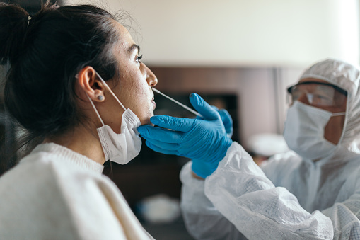 Médico en ropa de trabajo protectora tomando la prueba de hisopo de la nariz de la mujer joven photo