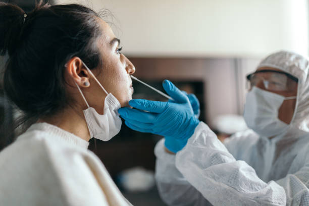 médico en ropa de trabajo protectora tomando la prueba de hisopo de la nariz de la mujer joven - covid 19 fotografías e imágenes de stock