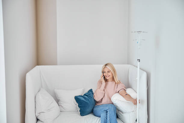 Woman undergoing intravenous vitamin therapy in a wellness center Merry female patient with a cellular phone sitting on the sofa during the medical procedure iv drip photos stock pictures, royalty-free photos & images