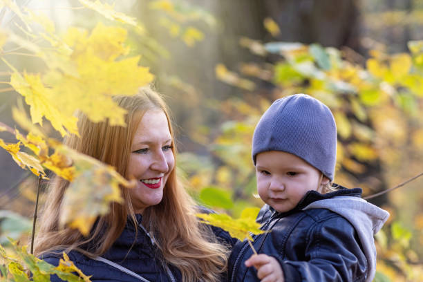 istock Young red haired mother and her son posing under maple tree outdoors closeup. 1285818459