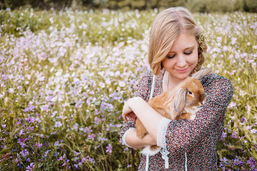Beautiful blond hippie girl with a little bunny in her arms in boho style. Creative color editing with added grain