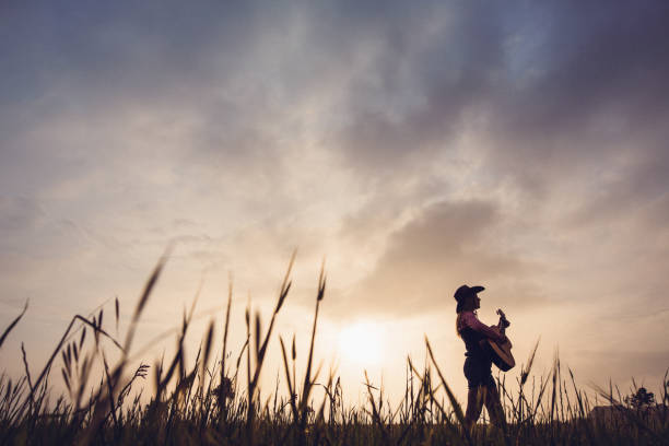 semi-silhouette d’une cowgirl avec une guitare dans le paysage pendant le lever du soleil - country music photos et images de collection