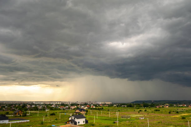 istock Moody landscape with dark stormy clouds with falling heavy downpour shower rain over distant town buildings in summer. 1285823902