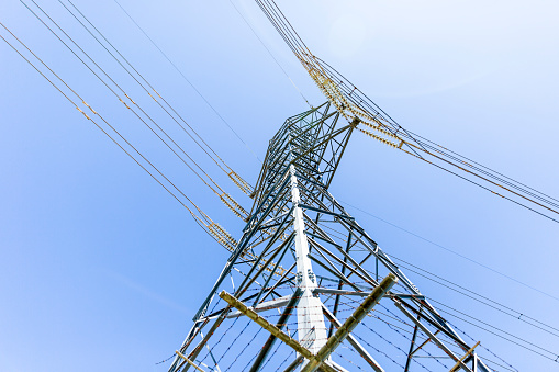 Low angle view of High voltage electricity pylon with overhead power lines, blue sky background with copy space, full frame horizontal composition