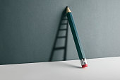 A pencil leaning against the wall. Ladder shade reflect on the wall.