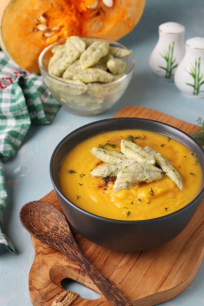 istock Pumpkin cream soup with cheese dumplings in dark bowl on light blue background, Vertical format, Closeup 1285827056