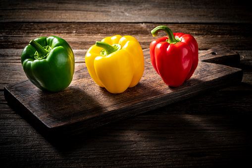 Three colorful bell peppers red yellow and green colors in a row on cutting boart at wooden rustic table