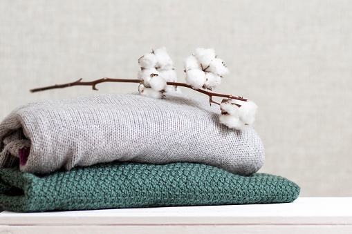 Stack of knitted warm clothes with cotton branch.