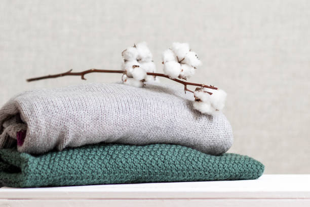 Stack of knitted warm clothes with cotton branch. stock photo