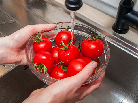 a woman's hand holds tomatoes under running tap water, the importance of handling and thoroughly washing vegetables and fruits during the covid-19 coronavirus pandemic