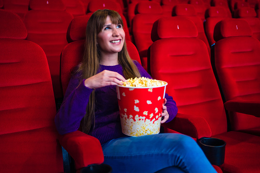 Young smiling woman with popcorn watching movie in the cinema theatre