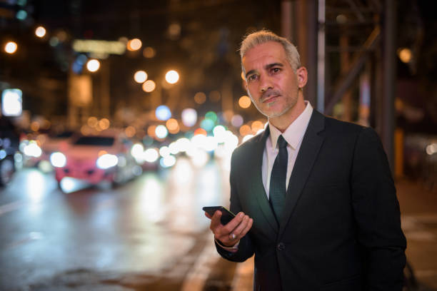 istock Businessman using mobile phone outdoors at night while waiting taxi 1285835030
