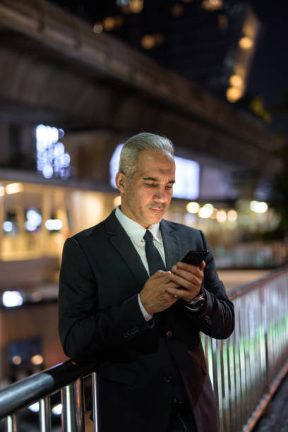 istock Businessman wearing suit in city at night while using mobile phone 1285835031