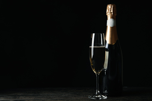 Bottle and glass of champagne on wooden table against black background