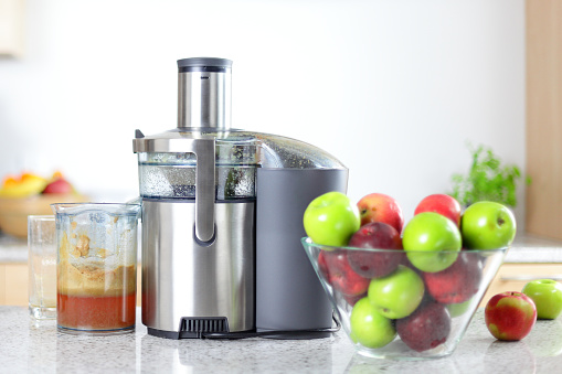 Apple juice on juicer machine - juicing concept. Apples in bowl in kitching and fresh pressed juice.